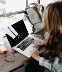 A young woman works remotely at a café, using her laptop and external hard drive.